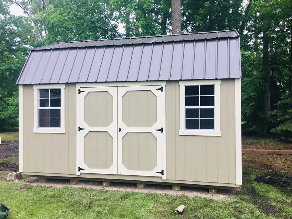 Tan lofted barn shed, gray metal roof, wooded yard