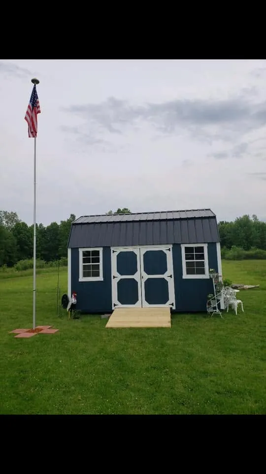 Navy lofted barn shed, white trim double doors, lawn with flagpole