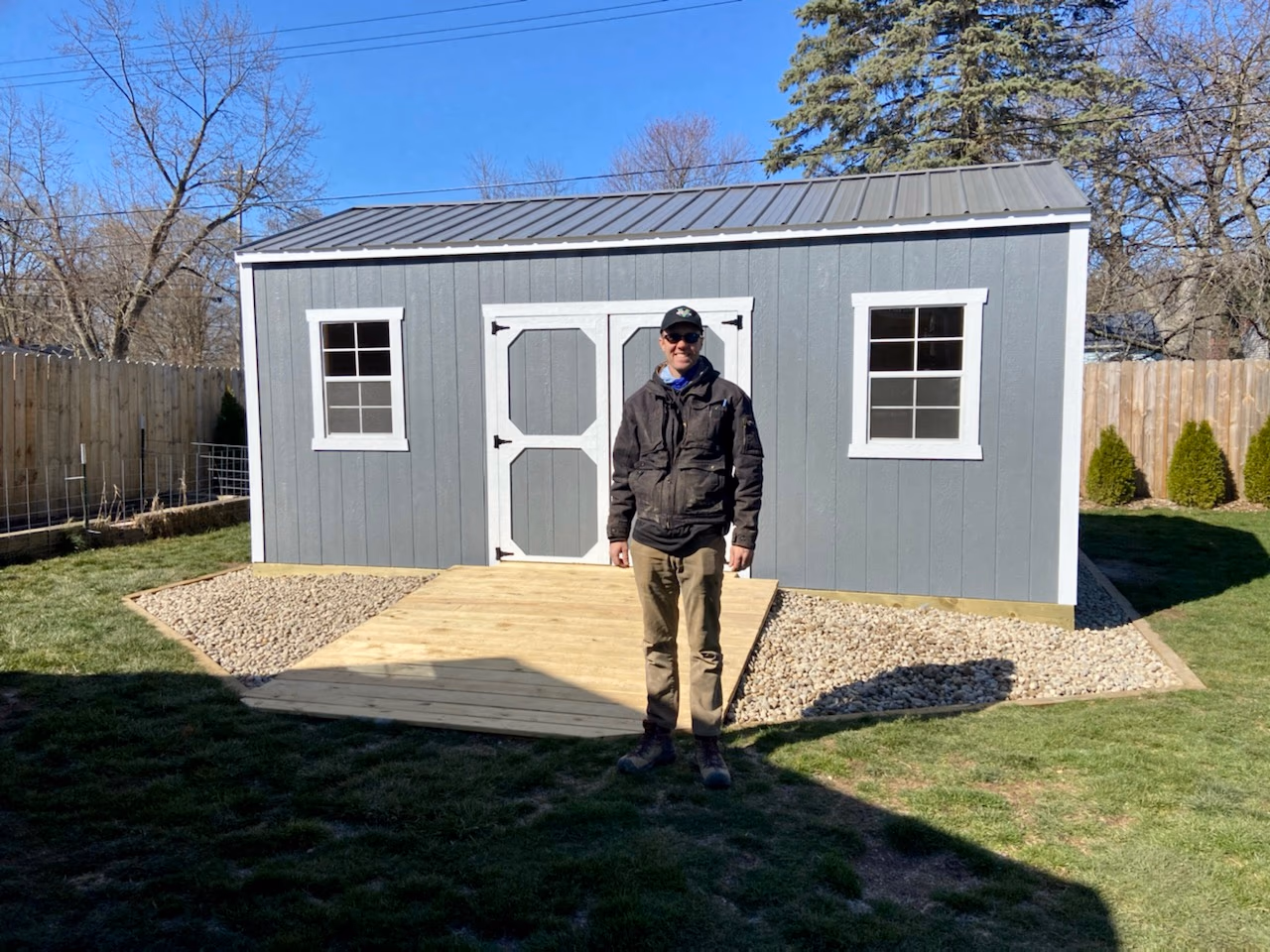 Customer smiling beside their new garden shed on delivery day