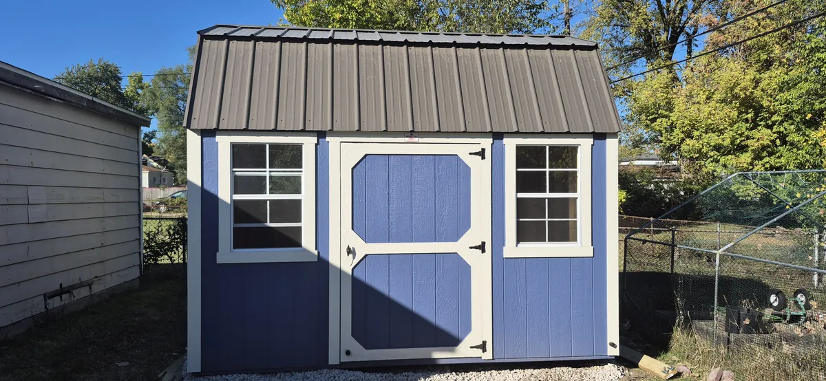 Periwinkle blue lofted barn shed with white trim and a brown metal roof in a backyard.