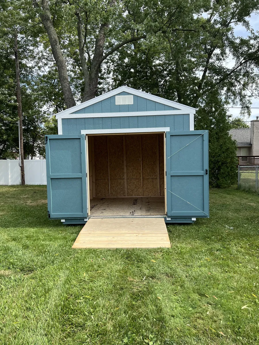 Blue utility shed with white trim and open double doors onto a wooden ramp in a backyard.