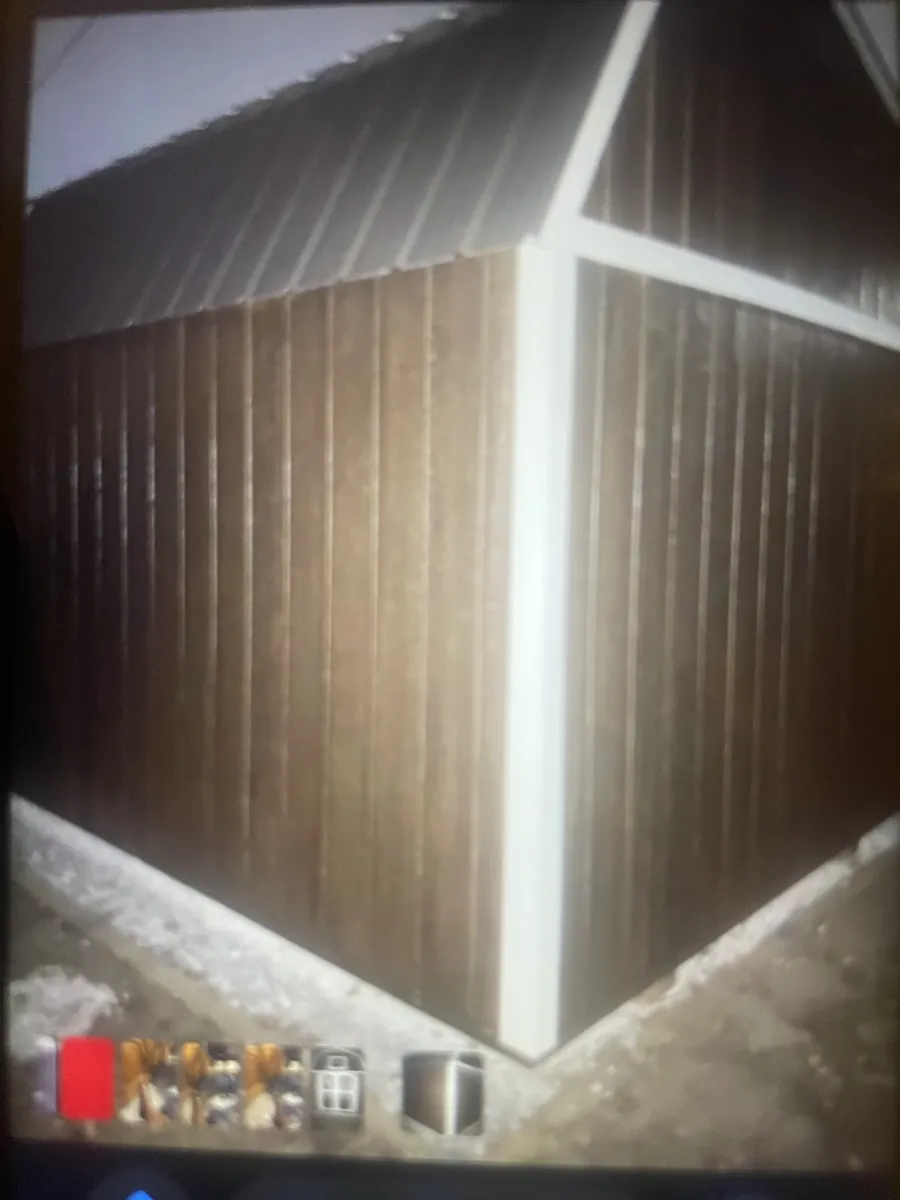 Photo of a screen showing the corner of a dark brown barn-style shed with white trim in light snow.