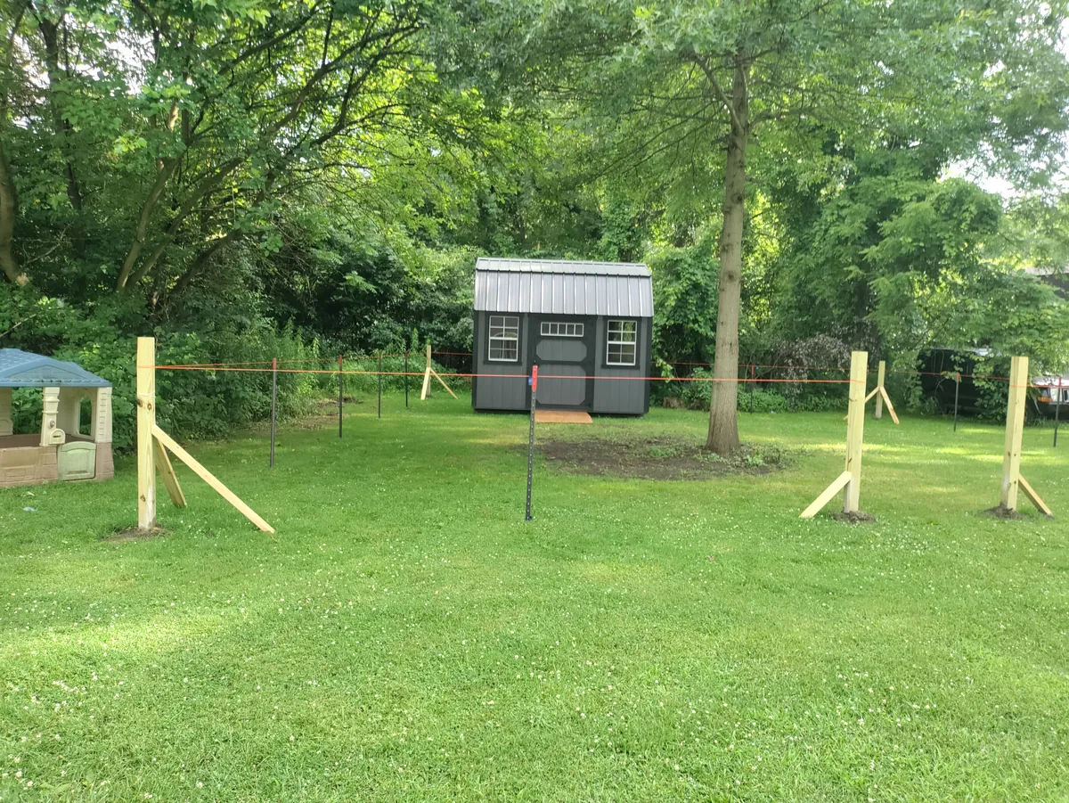 Dark gray shed with a metal roof in a backyard where new fence posts are being installed.