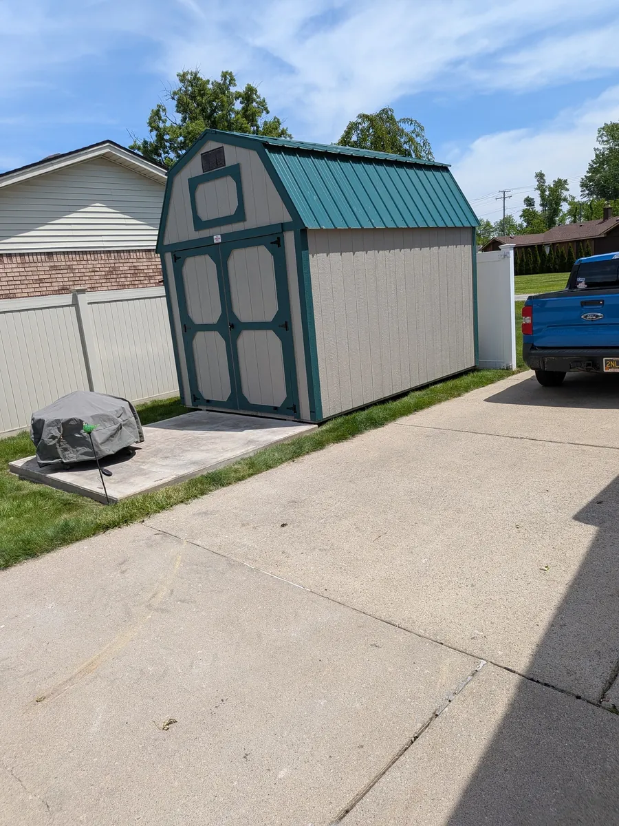 Gray lofted barn shed with green trim and a green metal roof beside a driveway.