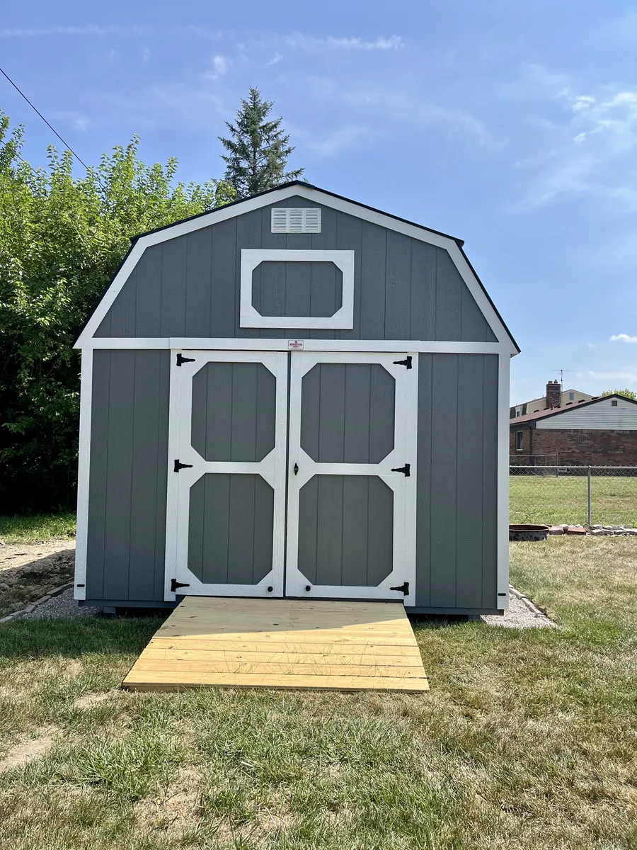 Gray lofted barn shed with white-trimmed double doors and a wooden ramp on a lawn.