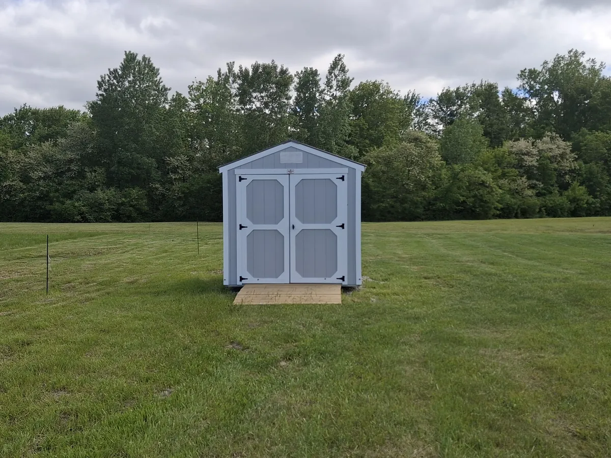 Light blue utility shed with double doors and a small ramp in an open grassy field.