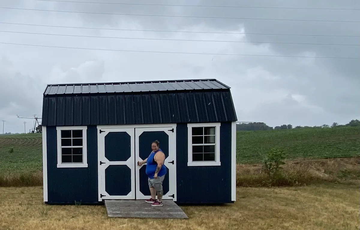 Navy lofted barn shed with white trim and double doors at the edge of a grassy field.