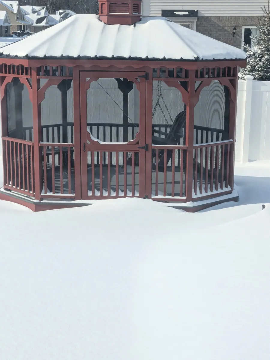Red gazebo with screened sides surrounded by deep snow.