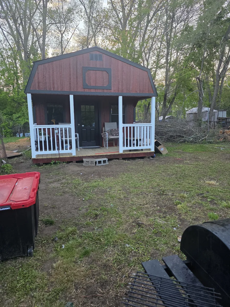 Red lofted barn cabin with front porch and white railings in a backyard.