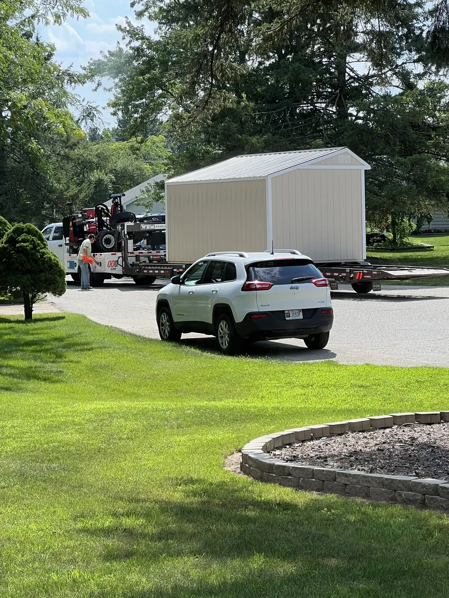 New cream shed on a delivery trailer being pulled into a residential driveway.