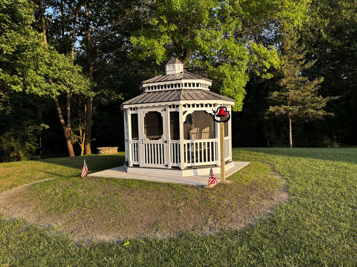 White vinyl gazebo with cupola and metal roof on a small mound in an open lawn.